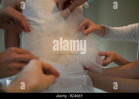 Des mains amies aider la mariée à s'habiller de sa robe. Banque D'Images