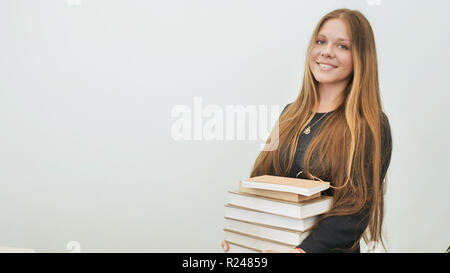 Une écolière de bonne humeur avec une pile de livres. Banque D'Images