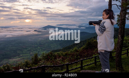 Femme touristes détenteurs d'un appareil photo reflex numérique à la recherche à la belle nature paysage de montagne dans le brouillard le soleil au lever du soleil d'hiver sur des points de vue à Ph Banque D'Images