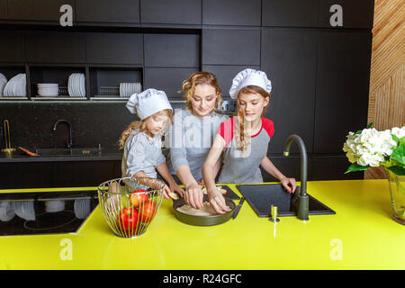 Famille heureuse dans la cuisine. La mère et les deux enfants de la préparation de la pâte, faire cuire la tarte aux pommes. Maman et les filles de la cuisson des aliments sains à la maison et avoir du plaisir. Chambre Banque D'Images