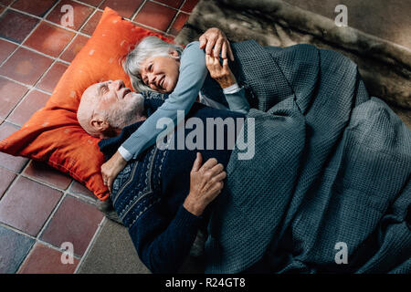 Senior couple allongé sur le sol se tenant et parler. Vieil Homme et femme dormir sur le plancher à la maison couvrant d'une couverture et de parler. Banque D'Images