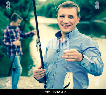 Portrait of cheerful man prendre du poisson frais sur les rives du lac Banque D'Images