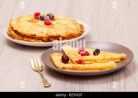 Crêpes maison garnie de framboises congelées et les mûres dans l'assiette et fourchette métallique sur fond de bois. Banque D'Images