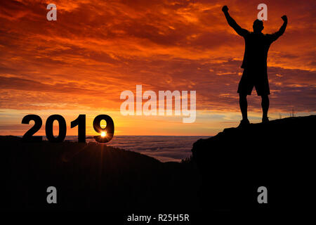 L'homme silhouette sur le sommet de la montagne en regardant le lever du soleil et 2019 ans alors qu'il célèbre. Banque D'Images