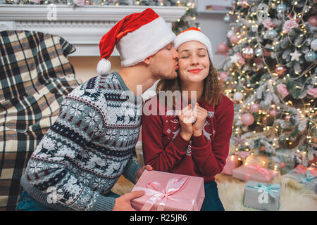 Belle photo de jeune homme embrassant une femme. Elle garde les yeux fermés et les poings ensemble. Elle aime ça. L'homme a présent dans les mains. Couple est décoré en ro Banque D'Images