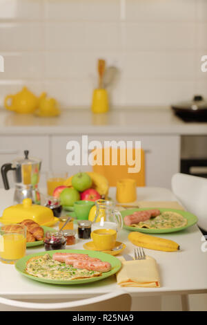L'heure du petit-déjeuner. Omelette aux verts et les saucisses. Des croissants et du jus d'orange, de la confiture. Café avec de la crème ou du lait. Fruits - bananes, pommes vertes et rouges. Banque D'Images