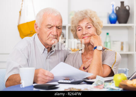 Couple frustrés face à des ennuis financiers table avec titres, espèces et calculatrice Banque D'Images