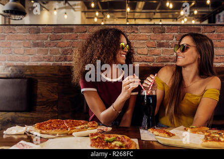 Les femmes élégantes portant des lunettes d'amis assis à restauration rapide. Deux femelles de boire un verre dans un café froid avec la pizza sur la table. Banque D'Images