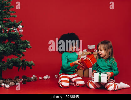 Enfants multiethnique à à leur cadeau de Noël. Heureux les petits enfants avec leurs cadeaux de Noël assis à côté d'un arbre de Noël. Banque D'Images