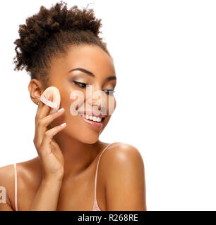 Charmante femme d'appliquer la poudre sur son visage d'appliquer des cosmétiques. Photo de femme afro-américaine avec une peau saine sur fond blanc. Les jeunes et Banque D'Images