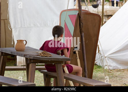 AQUILEIA, Italie - 22 juin 2014 : un jeune garçon en costume assis sur un banc en bois entre les tentes et des boucliers à l'échelle locale romaine ancienne r historique annuel Banque D'Images