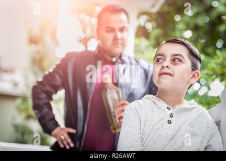 Peur et meurtri Mixed Race boy in front of Angry Man Holding bouteille d'alcool. Banque D'Images