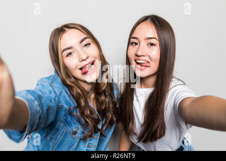 Portrait de deux femmes multiraciales joyeuse de noir et des cheveux blonds en tenant sur selfies smartphone, avec la langue, montrant la victoire plus isolé bl Banque D'Images