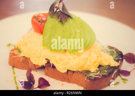 Oeufs brouillés, d'avocat, de pesto, tomates rôties, fromage "Grana Padano" sur brioche faite maison Banque D'Images