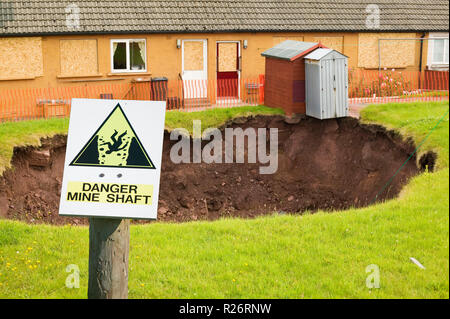 Un grand trou ouvert dans une maison jardin arrière de Egremont, Cumbria, Royaume-Uni, causés par la subsidence d'une ancienne mine de charbon Banque D'Images