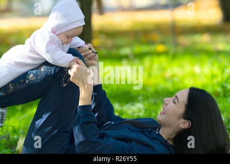 Mère jouant avec une petite fille balance son sur ses jambes alors qu'elle est de retour sur une couverture sur l'herbe dans un parc Banque D'Images