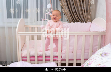 Un heureux, rires de bébé dans lit Bébé dans chambre rose scène. Banque D'Images