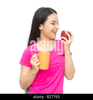 Portrait de jeune femme asiatique avec cuvette d'eau potable, thé ou café et une main tenant pomme rouge isolé sur fond blanc. Banque D'Images