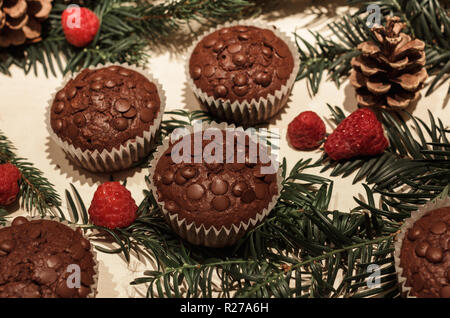 Cinq éclats de chocolat cupcakes en papier, quelques framboises parfait rouge, deux cônes de pin et quelques branches de pins verts Banque D'Images