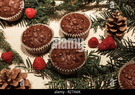 Cinq éclats de chocolat cupcakes en papier, quelques framboises parfait rouge, deux cônes de pin et quelques branches de pins verts Banque D'Images