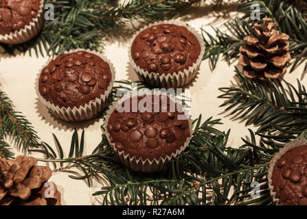 Cinq éclats de chocolat cupcakes en papier, deux cônes de pin et quelques branches de pins verts Banque D'Images