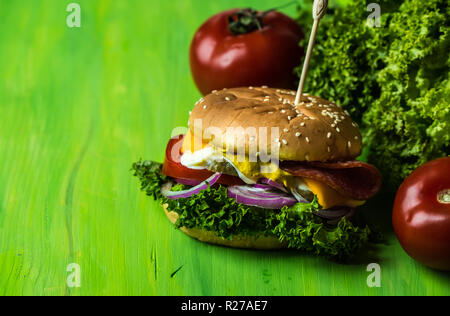 Délicieux cheesburger avec un grand nombre de légumes, moutarde, mayonnaise, de salami et d'oignon violet Banque D'Images