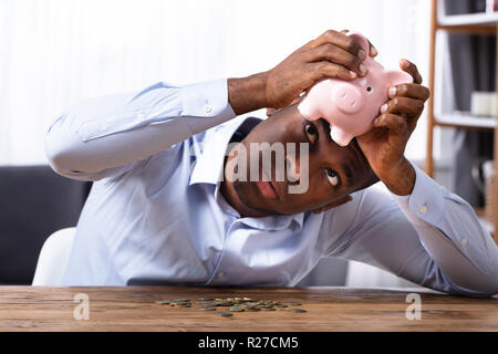 Contrôle de l'Afrique de l'homme dans l'épargne tirelire avec des pièces le bureau en bois Banque D'Images