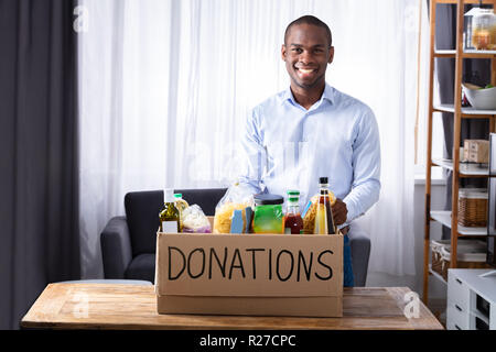Smiling Man Standing avec différents aliments en boîte de Donation Banque D'Images