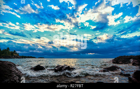 Confettis brillants nuages Lakeshore. Nuages colorés le ciel bleu au-dessus d'un éperon rive du lac Supérieur. Seascape background with copy space. Banque D'Images