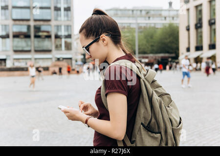 Une fille avec un sac à dos ou un étudiant sur un carré à Leipzig en Allemagne utilise un téléphone mobile pour afficher une carte ou appel ou pour une autre. Banque D'Images