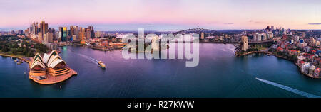 Pink le lever du soleil sur le port de Sydney, le Harbour Bridge et la ville les CBD sur les deux rives de l'antenne large panorama sur eaux calmes perturbés par les ferries et bo Banque D'Images