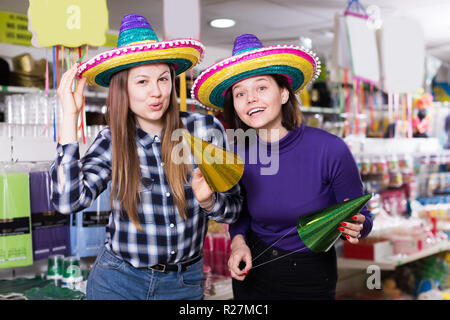 Smiling attractive deux filles essayant des chapeaux de fête dans la boutique d'accessoires de fête Banque D'Images