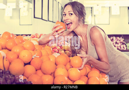 Jeune femme gaie positive l'achat des oranges sur la place de marché Banque D'Images