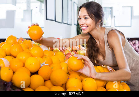 Smiling american female customer picking oranges sur le marché aux fruits Banque D'Images