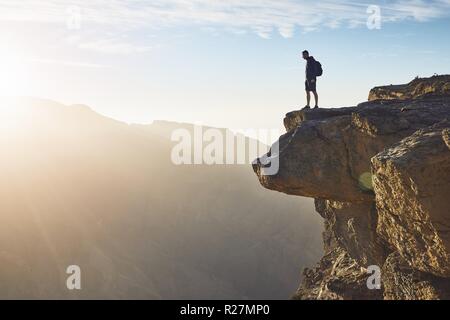 Jeune touriste avec sac à dos, debout sur le bord de la falaise au lever du soleil. Le Jebel Akhdar, Grand Canyon d'Oman. Banque D'Images
