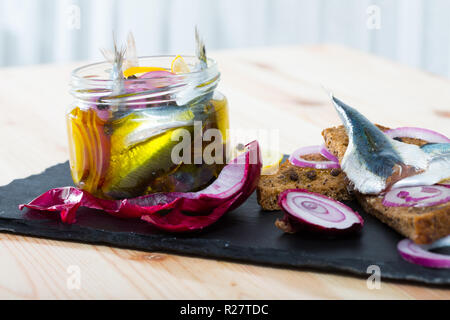 Pot d'anchois marinés maison avec l'oignon, betterave, poivron, vinaigre, citron, huile d'olive, sel de mer. Servi avec du pain de seigle sur la plaque d'ardoise Banque D'Images