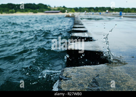 L'éclaboussure de vague sur jetty pier avec bornes métalliques. Au cours de la projection d'eau par temps couvert. Splash a gelé à l'embarcadère. USA, état du Michigan, Banque D'Images