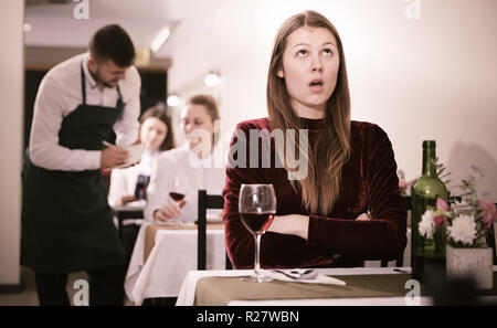 Femme élégante en colère s'attend à ce que l'homme pour le dîner dans le restaurant de luxe intérieur. Banque D'Images