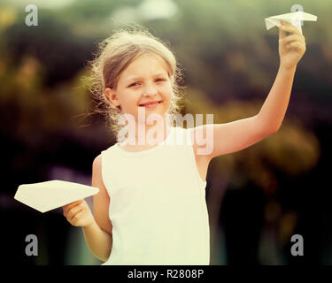 Smiling girl in elementary school age jouant avec le vol des avions en papier en plein air Banque D'Images