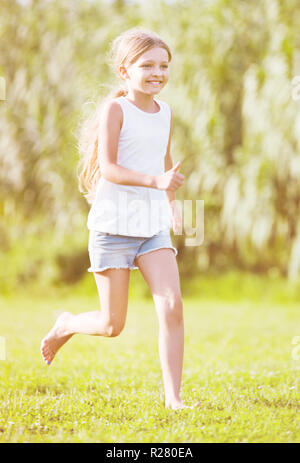 Heureux petit smiling girl in elementary school age tournant on Green grass in park Banque D'Images