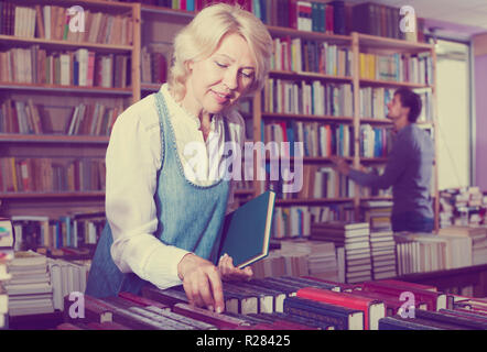 Femme mature à la recherche d'un nouveau livre sur les étagères de magasin de livre Banque D'Images