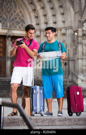 Deux touristes masculins sont la marche avec la carte et de valises et de photographier dans la rue à Barcelone. Banque D'Images