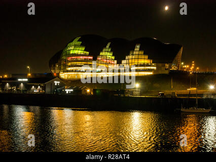 Newcastle Upon Tyne, Angleterre, Royaume-Uni, 17 novembre 2018. Vue depuis le quai le long de la rivière Tyne colorées de centre culturel Sage et salle de concert hall éclairé la nuit avec des reflets dans l'eau et la lune dans le ciel Banque D'Images