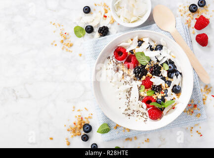 Bol de yogourt avec les baies fraîches, granola et chips de noix de coco servi sur fond de marbre blanc. Vue du dessus avec copie espace. L'horizontale. Banque D'Images