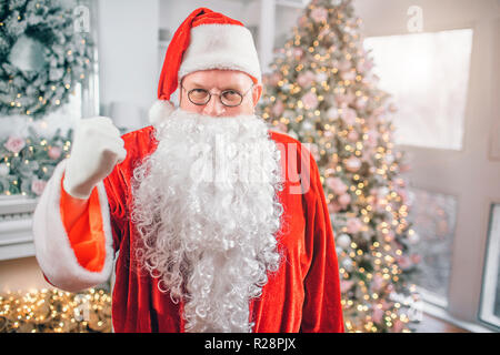 Photo du Père Noël se distingue et donne sur l'appareil-photo. Il montre le poing. L'homme menace. Il est dans la salle des fêtes. Banque D'Images