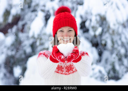 Jeune femme chandail tricoté en forme de coeur holding snow ball en hiver. Fille de famille lutte contre la neige jeu. En fait main tricot femme chapeau et mitaines avec C Banque D'Images