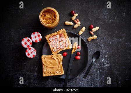 Toasts de pain avec beurre de cacahuète fait maison servi avec des tranches de canneberges fraîches Banque D'Images