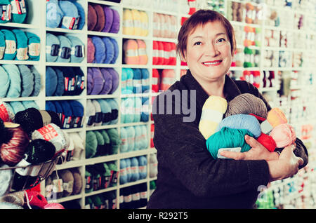 Portrait of woman holding positive tricoter les fils colorés dans les magasins d'arrière-plan Banque D'Images