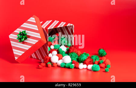 Cadeau de Noël fort sur le fond rouge, avec rouge, blanc et vert pompons. Banque D'Images
