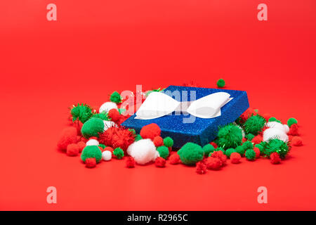 Blue Christmas gift box avec un arc entouré de rouge, vert et blanc pompons. Isolé sur fond rouge. Banque D'Images